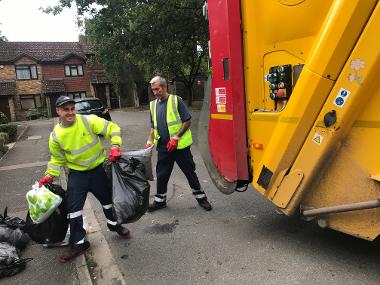 Photo of two waste collection crew members putting black rubbish bags in to a waste truck