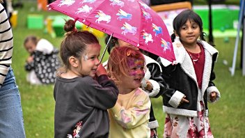 Two young girls with face paint smile while sheltering under an umbrella